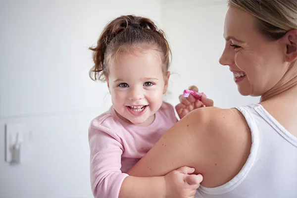 Photo of little girl smiling while her mom is holding her