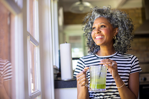 A beautiful Black woman smiling with celery smoothie in her hand