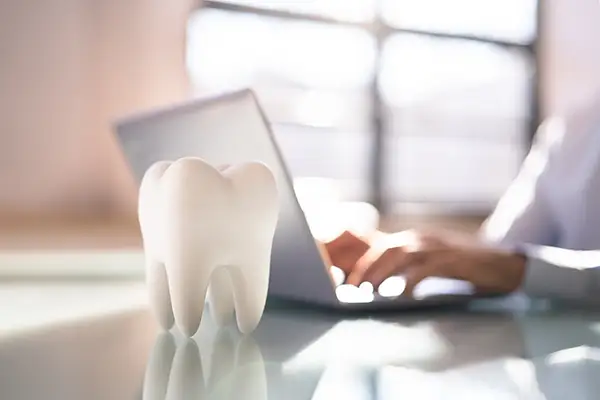 A person working on a dental blog on their laptop with a 3D tooth model on their desk.