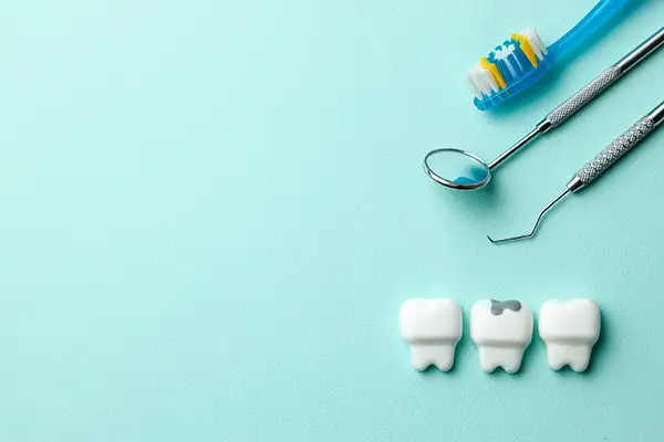 A minimalist setup of dental tools, a toothbrush, and three tooth models, with one showing a cavity.